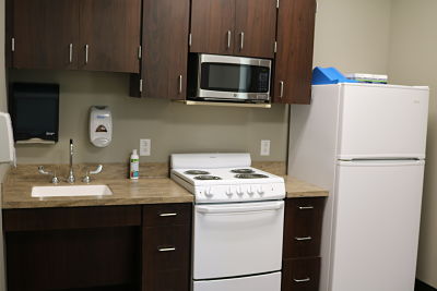 Active Daily Living kitchen to progress your ability to go home sooner.Occupational Therapy area showing a small kitchen that has a sink, cabinet spaces, stove and oven, fridge, microwave, countertops, paper towel dispenser, and soap.