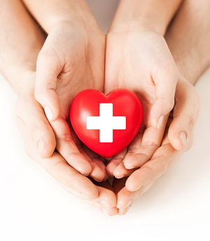 Family of three with their hands placed in one another, forming a heart. The child is holding a heart shaped object.