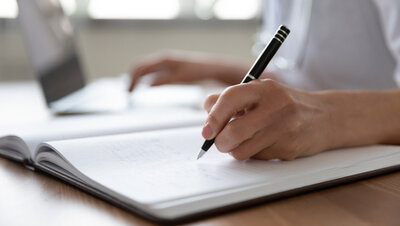 Female doctor holding a pen and writing in a notepad.