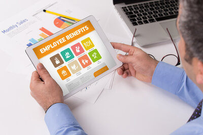 Male sitting at a desk holding a xtablet looking at employee benefits.